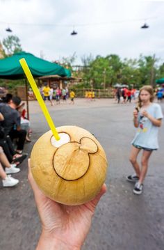 a person holding up a coconut drink with a smiley face drawn on it and a yellow straw sticking out of the top