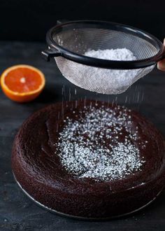 someone grating sugar on top of a chocolate cake with an orange in the background