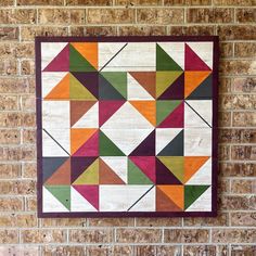 a wall hanging on the side of a brick building with an abstract quilt in it