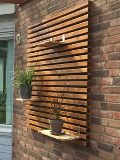 a wooden wall mounted planter on the side of a brick building with potted plants