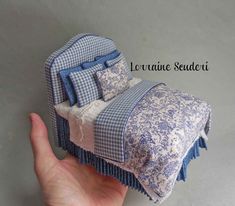 a hand is holding a miniature bed with blue and white bedspread on it