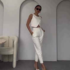 a woman standing in front of a white wall wearing sunglasses and a cropped top