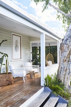 a porch with white furniture and plants on the deck area, next to a tree