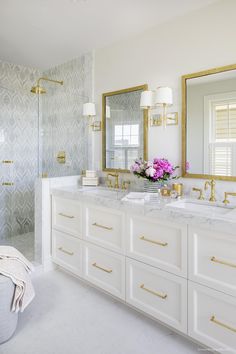 a white bathroom with gold trim and marble counter tops, along with two sinks in front of a large mirror