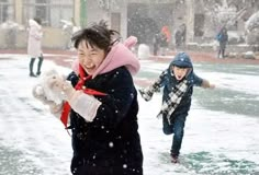 two children playing in the snow with one holding a teddy bear and another running behind them