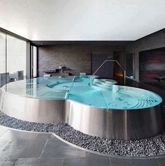 an indoor swimming pool in the middle of a room with large windows and stone flooring