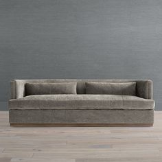 a couch sitting on top of a wooden floor next to a gray wall with two pillows