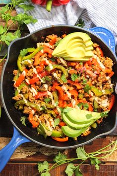 a skillet filled with meat, vegetables and avocado on top of a wooden table