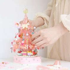 a woman is decorating a small pink christmas tree with beads and bows on it