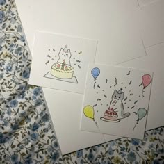 three birthday cards on a bed with blue and white flowers, one has a unicorn cake and the other has balloons