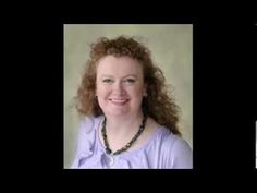 a woman with red hair is smiling at the camera and wearing a purple shirt that has beads around her neck