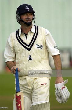 a male cricket player walking on the field with his bat in hand and helmet up