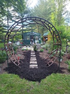 a garden with an arch made out of metal pipes and plants in the center, surrounded by mulch