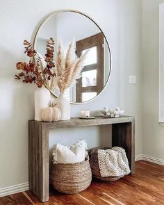 a wooden table topped with a round mirror next to a vase filled with dried flowers