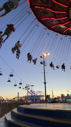 several people ride on swings and rides at an amusement park during the sunset or dawn