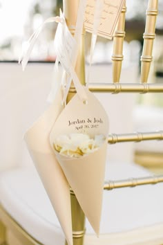 a wedding ceremony decoration with place cards and flowers on a gold metal chair backrest