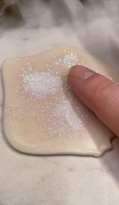 a finger touching a small white object with glitter on it