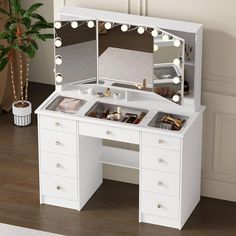 a white vanity with lights on it in a room next to a potted plant