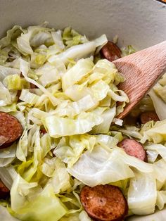 a wooden spoon in a bowl filled with cabbage and sausage