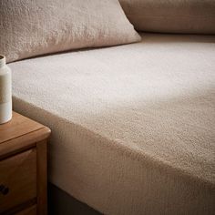 a white vase sitting on top of a wooden table next to a bed with pillows