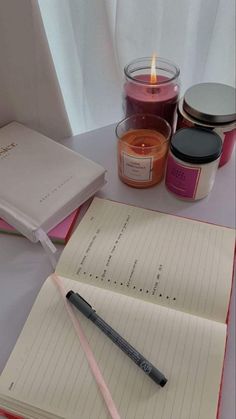 an open notebook sitting on top of a table next to a candle and some jars