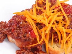 two hot dogs covered in chili and cheese sitting on a white plate with some bread