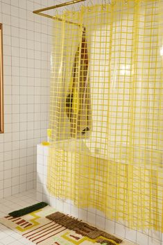 a yellow shower curtain in a bathroom next to a rug on the floor and tiled walls