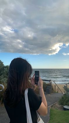 a woman taking a photo with her cell phone on the beach near the ocean,