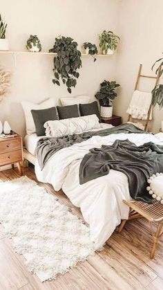 a bedroom with white and black bedding, potted plants on the wall and wooden flooring