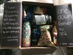 an open box filled with snacks on top of a white sheet covered bed next to a chalkboard sign