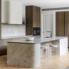 a large kitchen with marble counter tops and wooden cabinets, along with two stools