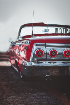 an old red car parked in a parking lot next to another car with the license plate on it's hood