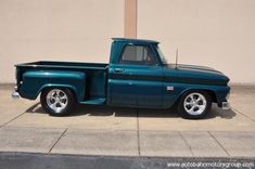 a blue truck parked on the side of a road next to a building with a tan wall