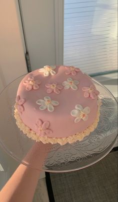 a cake with pink icing and white flowers is being held by a woman's hand