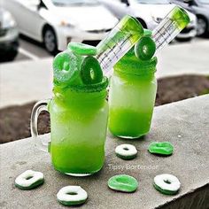 two glasses filled with green liquid sitting on top of a cement table next to donuts