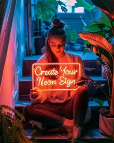 a woman sitting on the stairs holding a neon sign that says create your neon sign