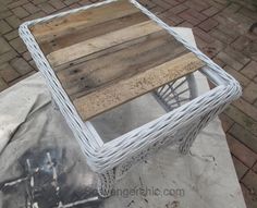 a white wicker table sitting on top of a cement floor next to a brick sidewalk