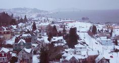 a city with lots of snow on the ground and houses in the foreground, and a bridge across the water