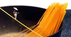 a black bowl filled with yellow noodles and a person holding an umbrella on top of it