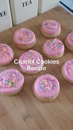 twelve cookies with pink frosting and sprinkles on a wooden table top