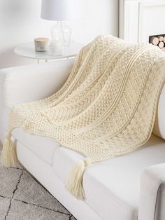 a white couch with a blanket on top of it next to a table and lamp