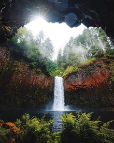 a waterfall is seen from the inside of a cave with sunlight coming in through it