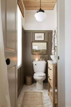 a white toilet sitting inside of a bathroom next to a wooden ceiling mounted above a sink