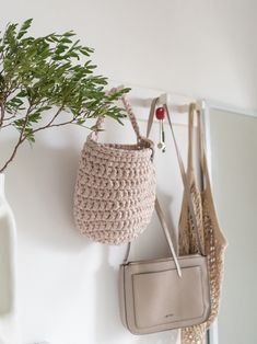 two purses hanging on the wall next to a potted plant in a vase