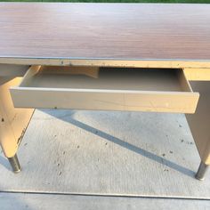 a wooden desk with two drawers sitting on top of the floor next to a grass area