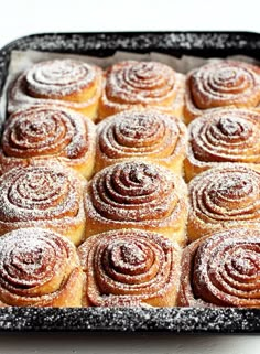 a pan filled with cinnamon rolls covered in powdered sugar on top of a table