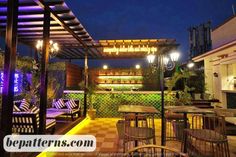 an outdoor seating area at night with lights on the ceiling and tables in the foreground