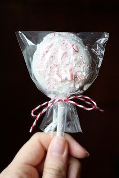 a hand is holding a candy cane wrapped in plastic wrapper with white frosting and red sprinkles