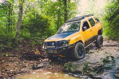 a yellow four - doored truck is driving through the mud on a trail in the woods