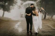 a bride and groom walking in the rain under an umbrella